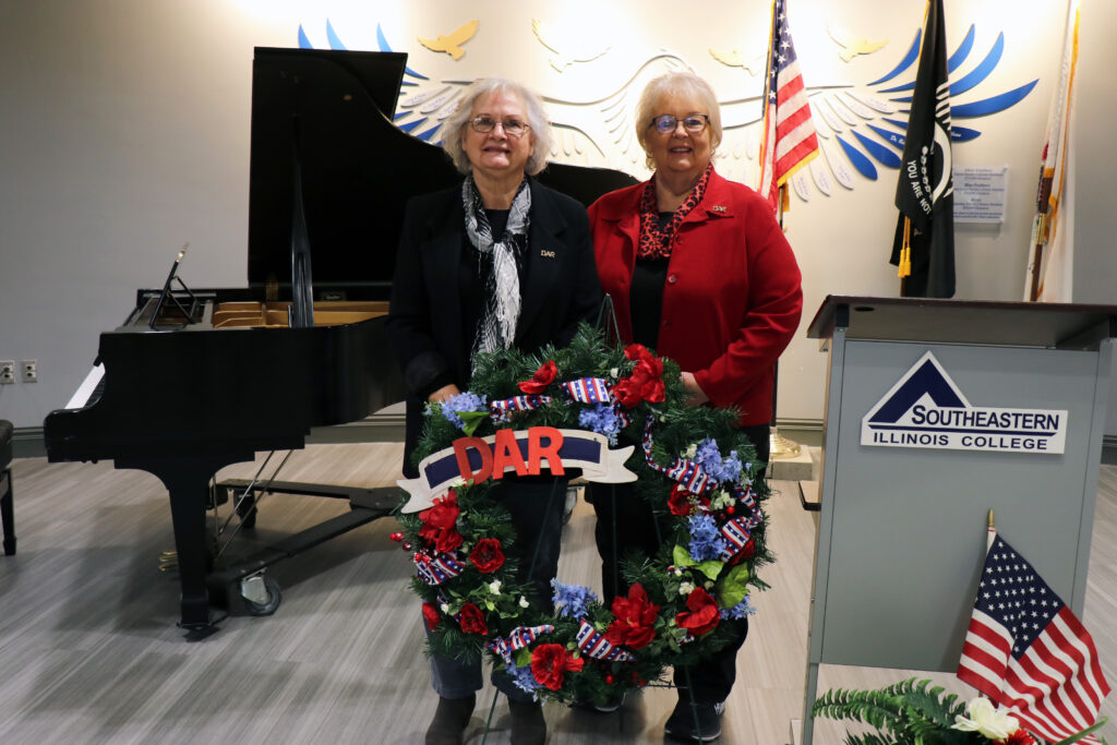 Cheri McClusky and Rhonda Oglesby of the Michael Hillegas Chapter of the Daughters of the American Revolution stand with the remembrance wreath they laid during the ceremony at Southeastern Illinois College.